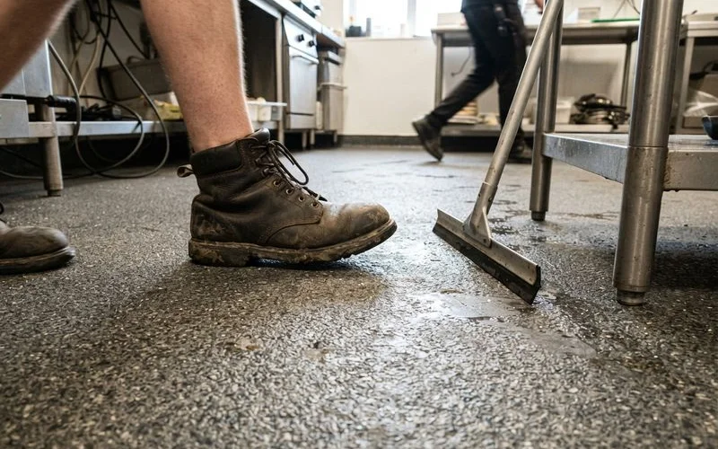 Close-up of a textured, slip-resistant epoxy floor coating in a commercial kitchen or warehouse setting showing visible aggregate texture
